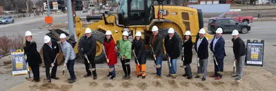 A photo of people standing in a line with shovels in front of a machine for a groundbreaking event