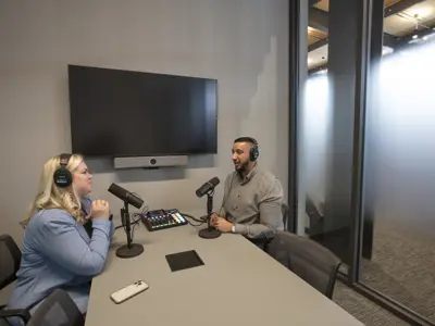2 people are recording a podcast in front of microphones
