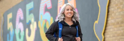 A woman stands in front of a 56560 mural