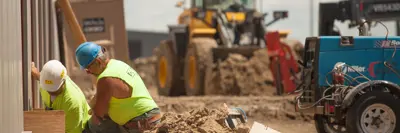 2 construction workers are working in the dirt with machines behind them