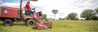 An employee mows grass with the water tower in the background