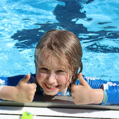 A photo of a smiling kid swimming in the pool 