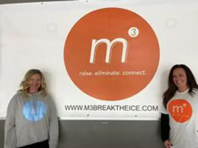 Lezlee Bertie & Amber Ferrie stand by a logo m3