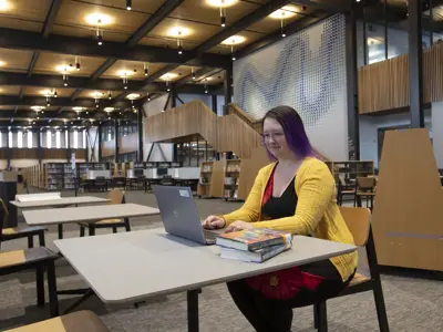 A person sitting at a table with a laptop with the library behind her