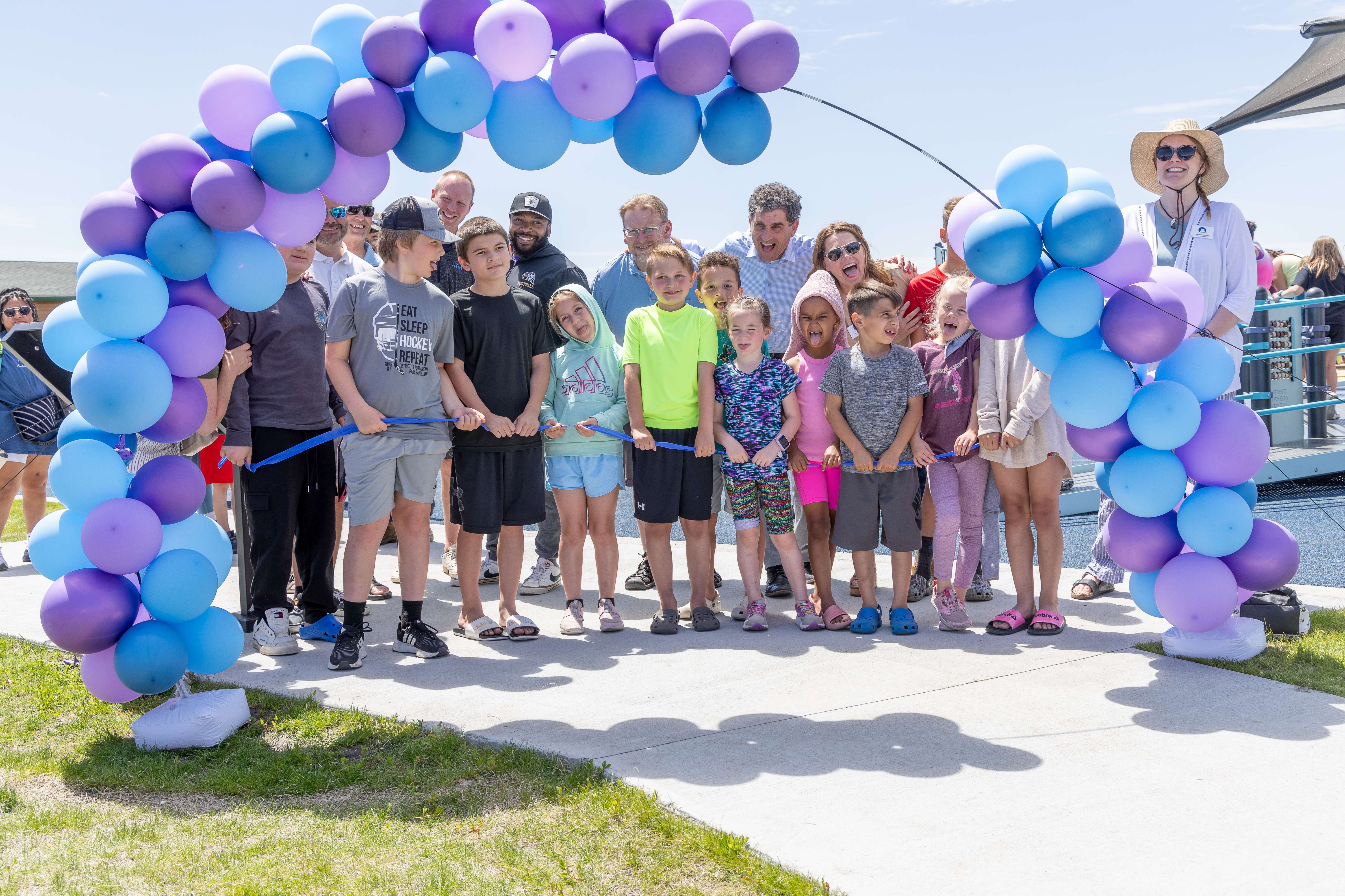 Kids are under a balloon arch for a ribbon cutting at a playground